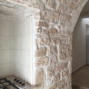 In the foreground there is the bare stone wall of the kitchen, in the background there is a section of the corridor