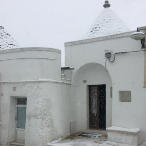 Foto dell'ingresso del trullo con un manto di neve sopra il cono e i marciapiedi